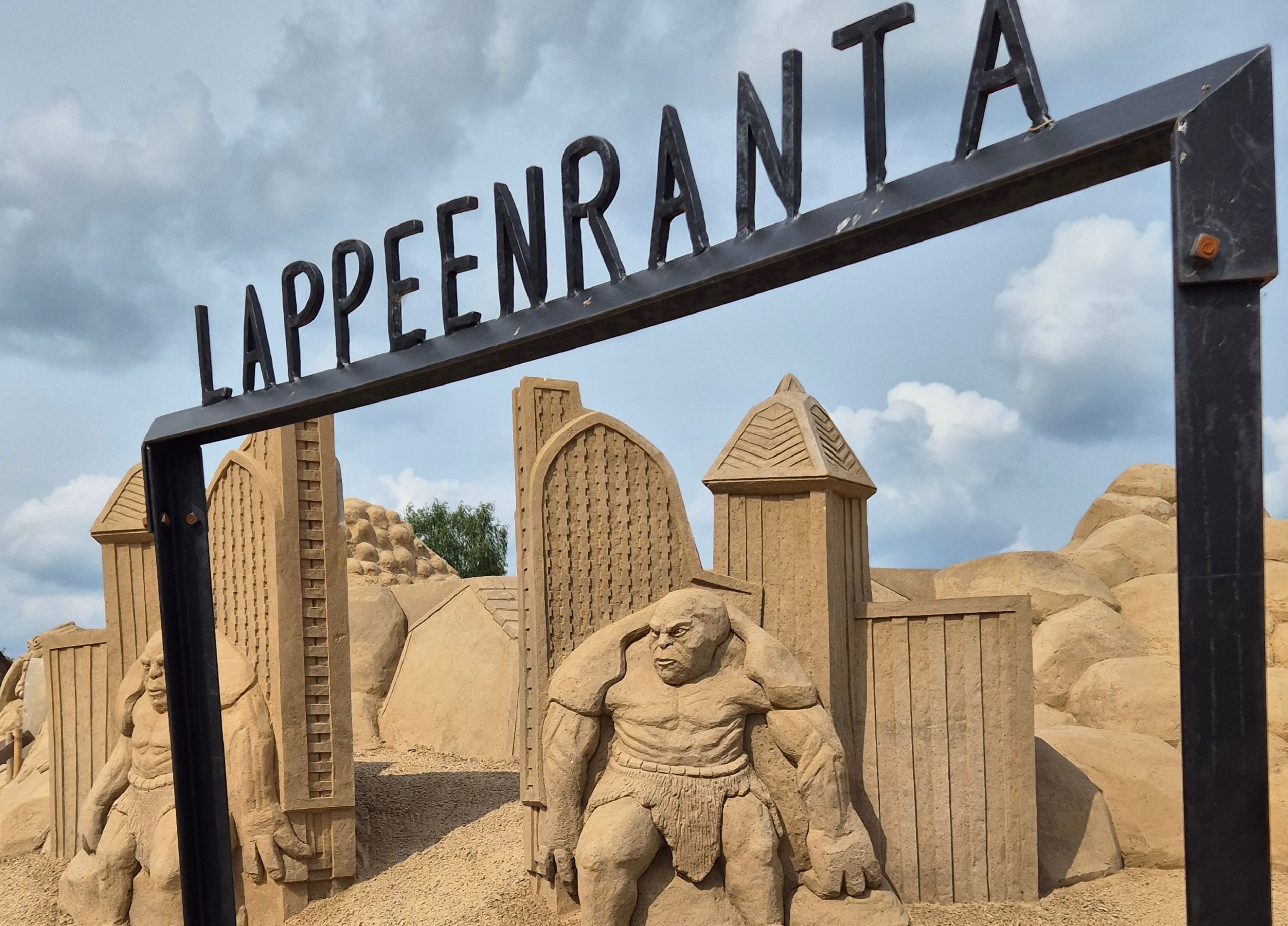 Etualalla rautainen portti, jonka päällä teksti Lappeenranta. Taka-alalla hiekasta muotoiltu linna ja örkkejä.